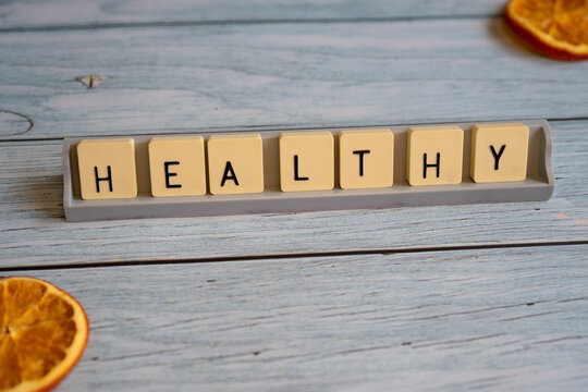 Letter tiles forming the word -Healthy- on a weathered wooden surface, accompanied by dried orange slices. Concept of health, nutrition, wellness, and balanced living.