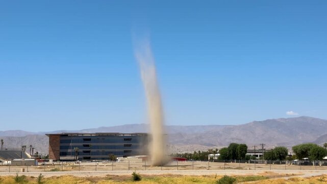 Large dust devil whirlwind spinning across a desert lot near mountains