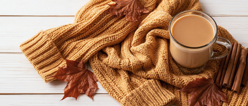 Warm cozy knitted sweater with cup of hot coffee and autumn leaves
