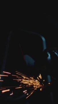Man working at factory cuts metal with a grinder. Male at a construction site cuts off piece, bright flying sparks and particles of material fly. Guy Industrial worker use angle grinder cutting metal