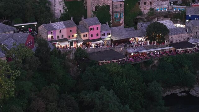 Aerial view of the historic Old Bridge (Stari Most) surrounded by traditional stone buildings, historic towers, and red-roofed houses in the old town at dusk in Mostar, Bosnia and Herzegovina