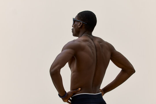 Muscular man poses with hands on hips in simple studio backdrop