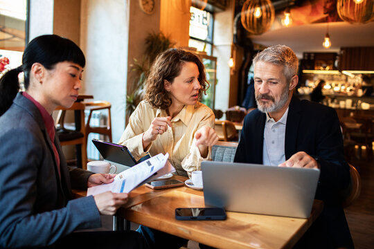 Three colleagues reviewing data on a laptop in a cafe