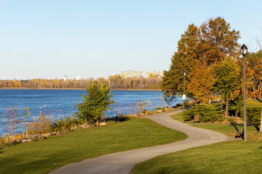 Shoreline walkway with autumn trees on sunny day in Andrew Haydon Park in Ottawa, Canada. Winding paved trail along Ottawa River waterfront