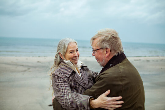 Smiling senior couple hugging on a windy beach