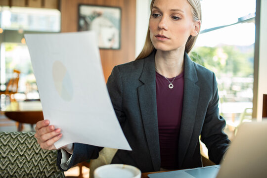 Woman analyzing printed report at cafe with laptop