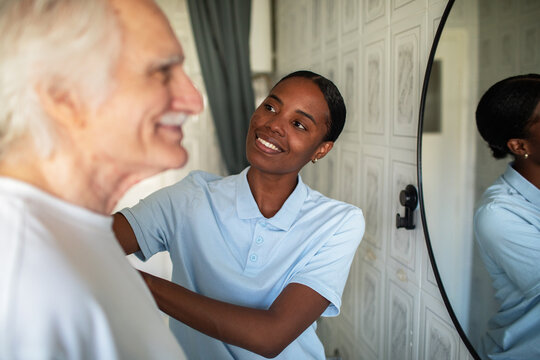 Caregiver helping senior man get dressed at home
