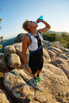 Runner drinks water on rocky mountaintop during sunset