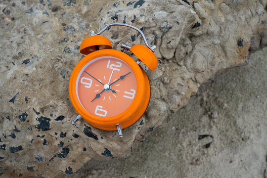 Orange alarm clock on rough stone surface for time management and daylight saving time concept	
