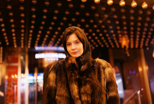 Woman in Fur Coat Stands Under Bright Lights at Night