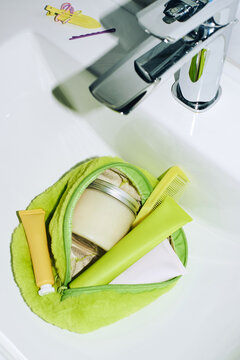 a green toiletry bag with creams in the sink