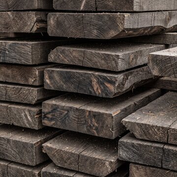 Stacked dark weathered wooden planks and thick timber boards with natural tree rings and rough cut cross sections
