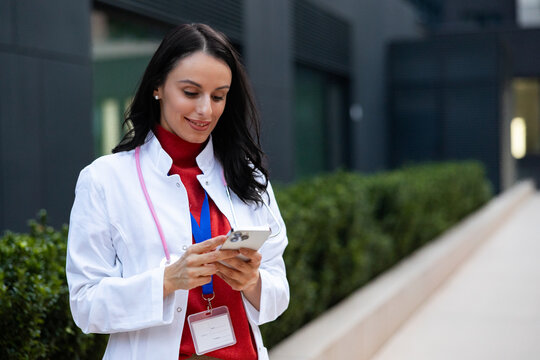 Female doctor using smartphone for teleconsultation outside medical building, connecting with patients and managing healthcare communications digitally