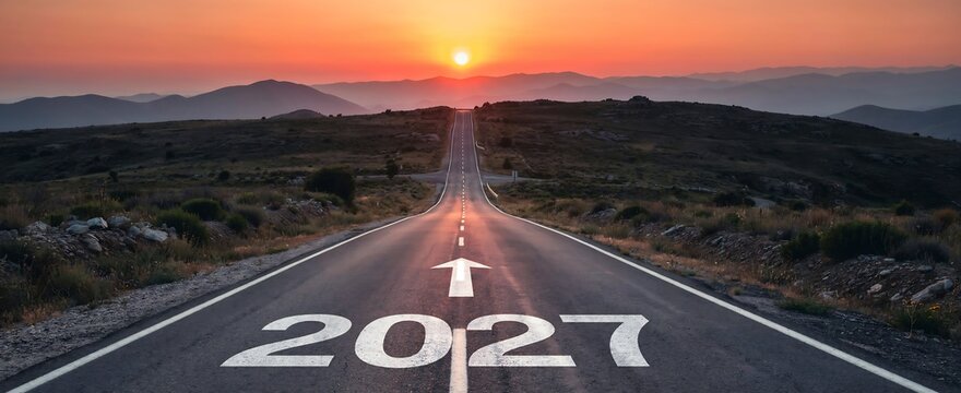 Straight road leading toward glowing sunset over mountains with 2027 text and directional arrow on asphalt for concept of future goals and upcoming year journey.