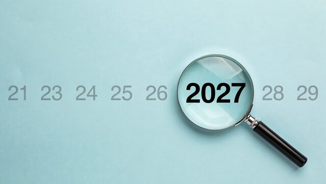 Magnifying glass focuses on the year 2027, highlighting it from a sequence of years on a light blue background, symbolizing future planning or research.