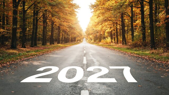 Year 2027 on asphalt highway surrounded by autumn forest canopy with warm golden light for future perspective and new year business goal setting background designs.
