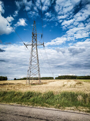 Obraz premium High voltage power line pylon in a rural wheat field in Poland under a cloudy blue sky