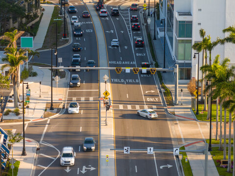 Dynamic street scene in Sarasota with people walking across a pedestrian crossing while traffic lights control the flow of vehicles at a busy junction.