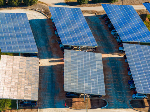 Solar panels installed as shade roof over parking area with parked cars for effective generation of clean electricity. Photovoltaic technology integrated in urban infrastructure.