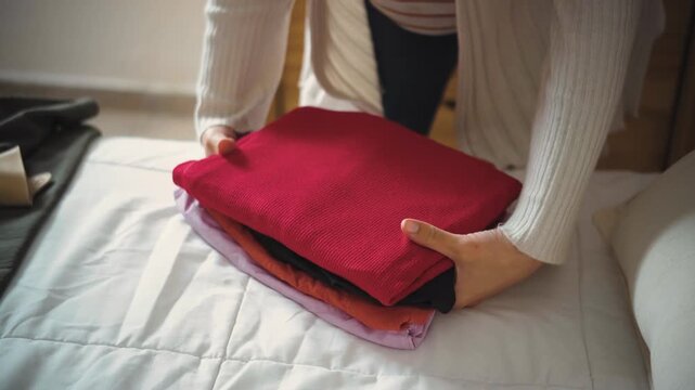 Close-up of a young woman&rsquo;s hands folding and organizing clothes on her bed before putting them away in her closet. Concept of home organization and daily routines.
