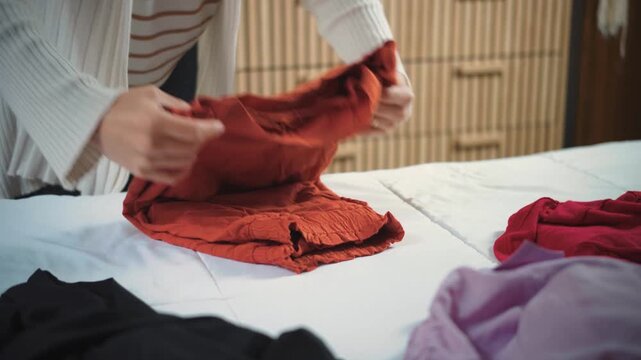Close-up of a young woman&rsquo;s hands folding clothes on her bed before storing them in her closet. Concept of home organization and daily household routines.
