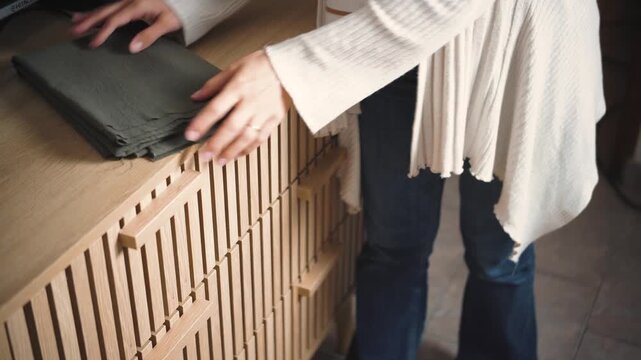 Young woman putting a blanket away in a bedroom dresser drawer. Concept of home organization, storage solutions, and everyday household routines.
