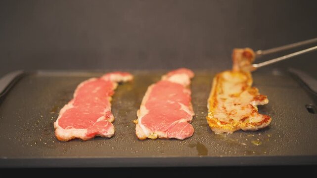 Cocinando y volteando tiernos filetes de ternera en una plancha el&eacute;ctrica caliente en la cocina