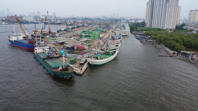 Aerial drone view of a busy harbor during the afternoon, showing numerous vessels navigating near the port while large ships remain docked along the waterfront, high