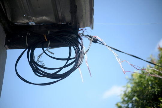 Coiled electrical cable tied under metal roof eave against clear sky