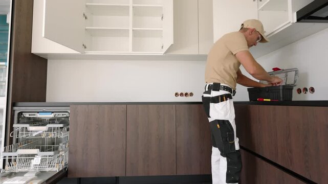 Kitchen installer selecting tools beside open wall cabinets