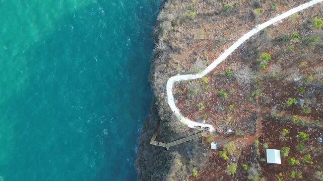 Aerial drone video flying over turquoise sea and rocky cliff coastline with winding white path on Gili Iyang, Pulau Oksigen, Sumenep, Madura, East Java, Indonesia