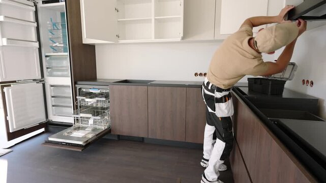 Worker fitting a kitchen extractor hood beneath wall cabinets