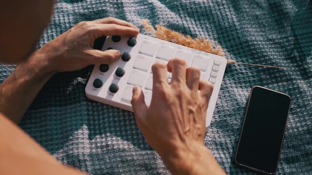 Beatmaker taps rhythmic patterns on portable electronic synth pads during an outdoor creative session. Tactile finger drumming showcases expressive mobile music production.