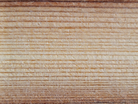 Close-up texture of a machine-processed wooden board with parallel cutting marks and natural wood grain. Rough timber surface with horizontal lines, beige and brown tones, woodworking background.
