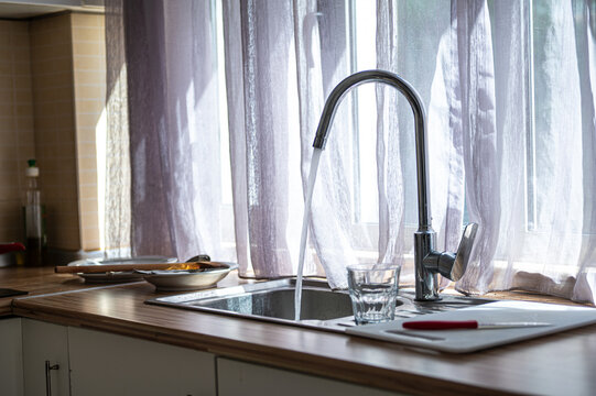 Kitchen sink and faucet beside a curtained window in a home during daylight