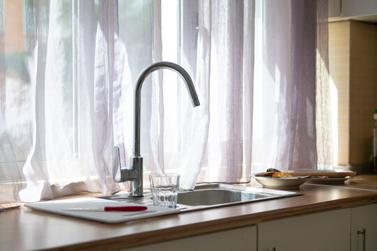 Kitchen sink and faucet beside a window with sheer curtains in daylight