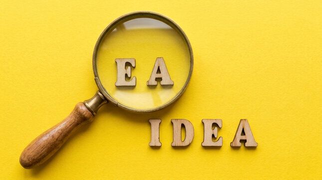 Magnifying Glass on Wooden Letters EA with IDEA nearby on yellow background Concept of discovery research and innovation