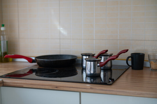 Pans and a cooking pot arranged on a kitchen cooktop beside a tiled wall