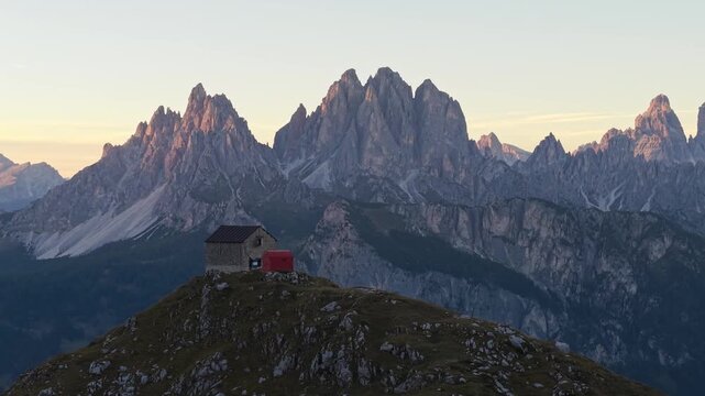 Aerial 3x telephoto view of Rifugio Tiziano and Bivacco Toso at sunset in the Marmarole Dolomites, with Tre Cime di Lavaredo in the background.