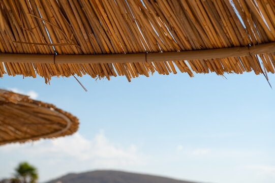 Thatched bamboo parasols frame a mountain view beneath the daytime sky