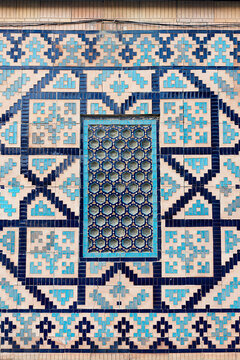 Geometric tilework and lattice window detail on Sher Dor Madrasah at Registan Square in Samarkand. Intricate mosaic patterns in turquoise and navy blue decorate the historic facade. Ideal for travel.