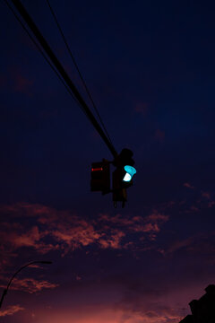 A green signal hangs from cables against a New York dusk sky. Overhead cables lead to a traffic light with small clouds above a narrow strip of orange horizon.
