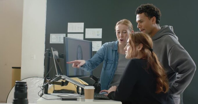 Diverse coworkers following woman in denim at studio pointing at monitor, refining layout