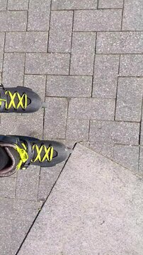 Vertical POV close up of inline skater riding on grey concrete sidewalk tiles 