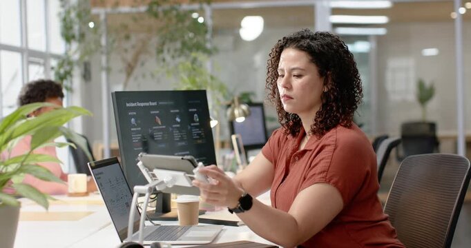 African American woman adjusting tablet, typing on laptop and handling incidents at shared desk