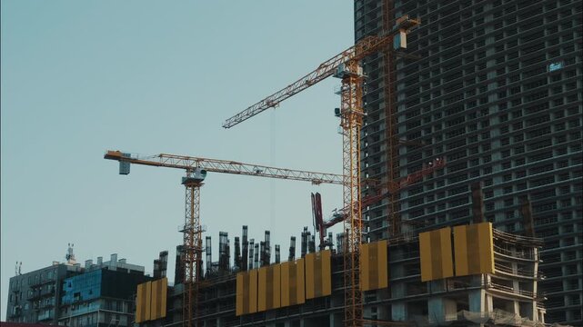 Tower cranes rotating at construction site in timelapse, heavy machinery operating beside unfinished high rise building and exposed concrete columns, structural engineering and urban development.