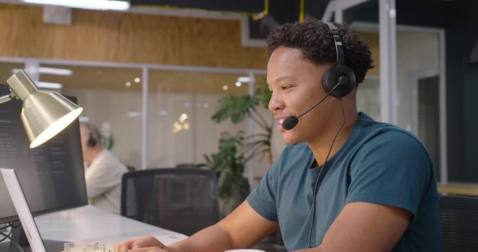 Coworkers watching African American man taking support call talking on headset using laptop noting