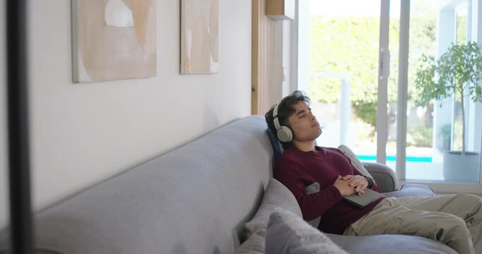 African American man 20s ending tablet wearing headphones leaning back on sofa resting, copy space