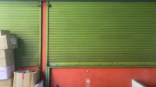 Storefront Closure and Logistics Storage: Closed Green Rolling Shutter Gate with Stacked Cardboard Delivery Boxes