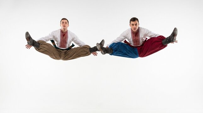 Two men in traditional Ukrainian Cossack costumes performing a dynamic jump in mid-air